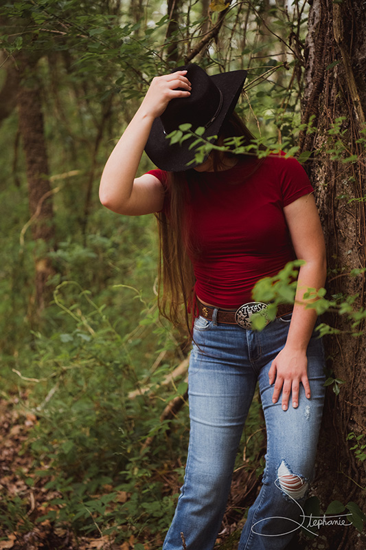 A cowgirl resting against a tree.